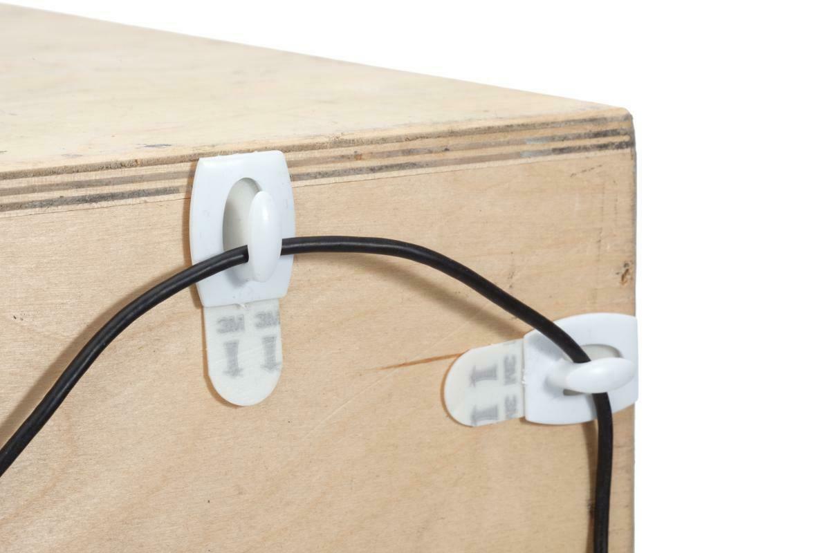 Se muestran las guías para cables de la marca Command adheridas a la parte posterior de un escritorio de madera con un cable atravesado por ellas