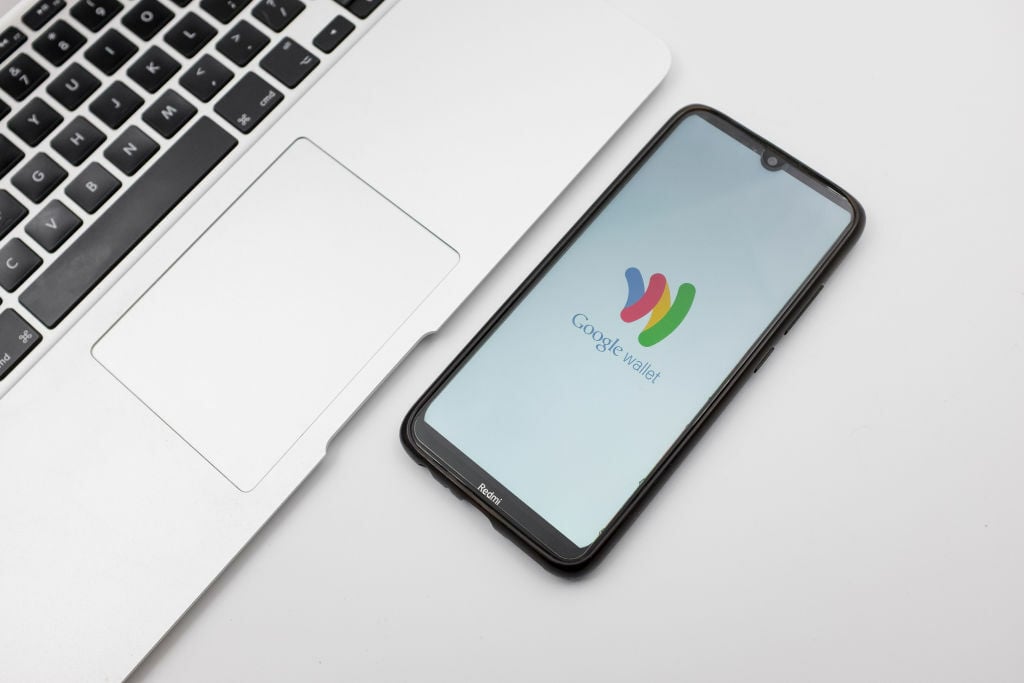 teléfono inteligente que muestra el logotipo de Google Wallet sentado en un escritorio junto a una computadora portátil abierta